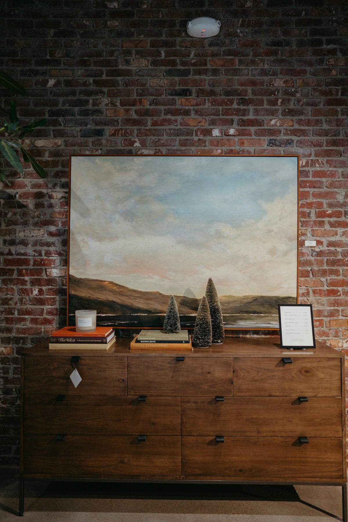 a painting hangs on a brick wall above a dresser