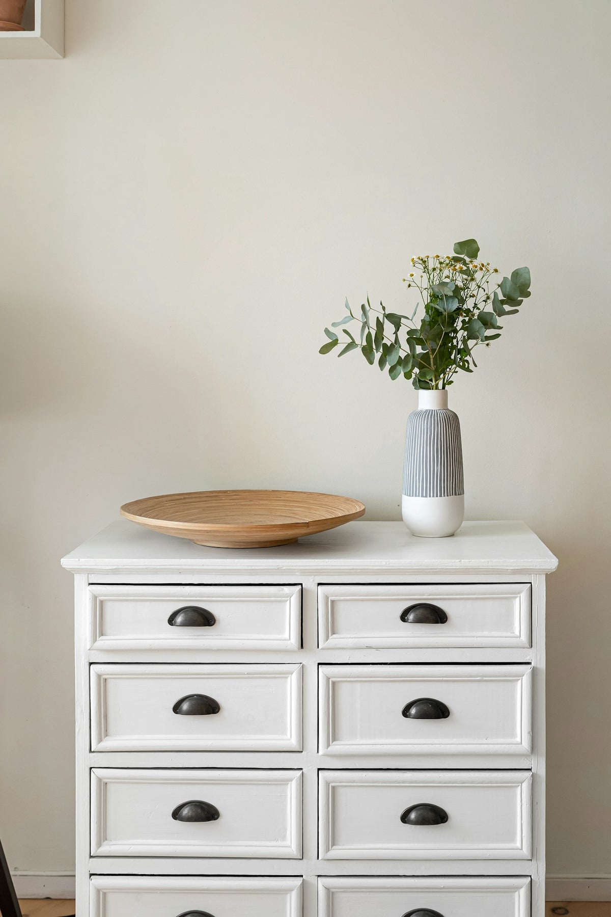 A white dresser with a wooden bowl on top of it