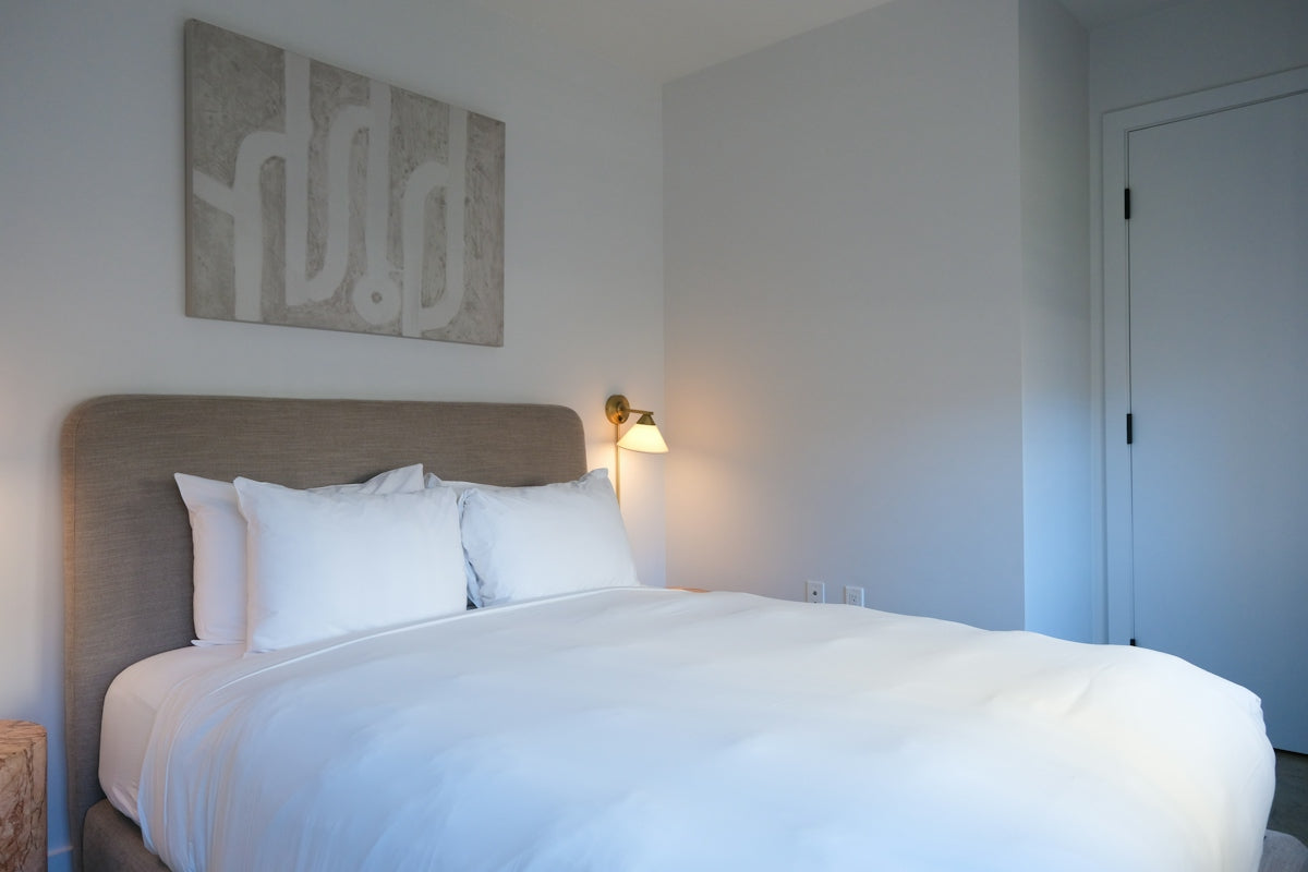 A neatly made bed with white linens and pillows.