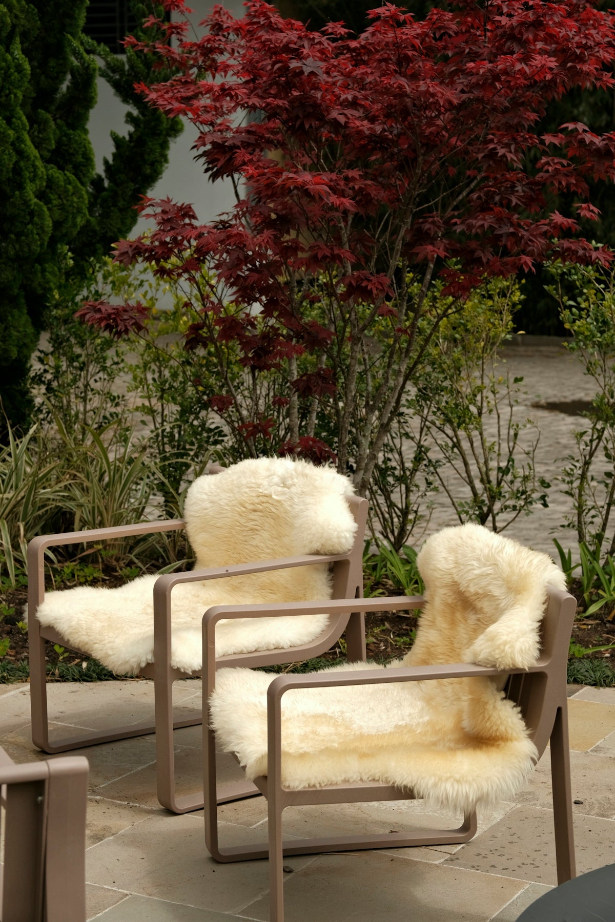 Two chairs with sheepskin throws in garden.