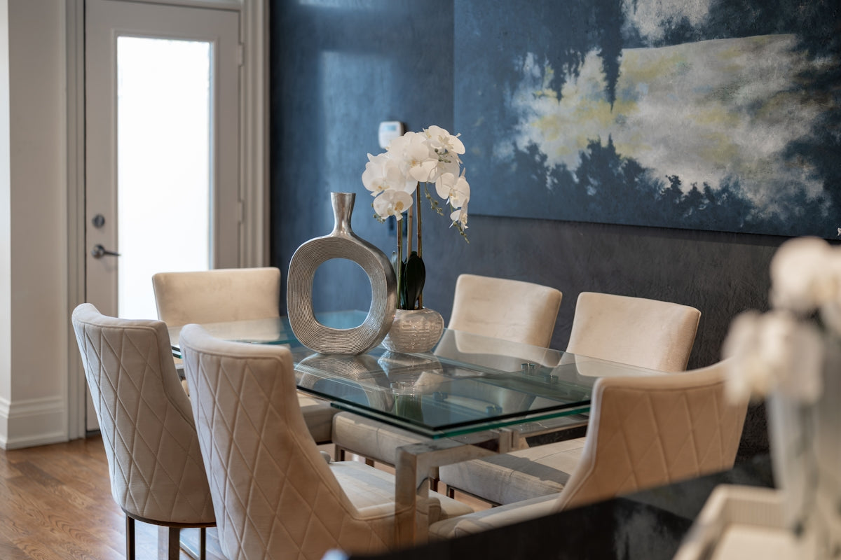 Elegant dining room with glass table and upholstered chairs.