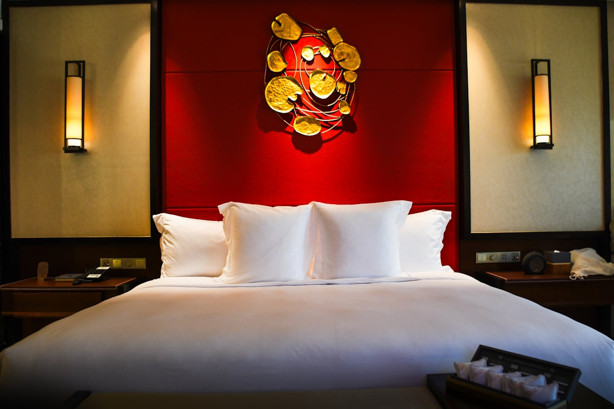 Luxurious hotel bed with red accent wall and art.
