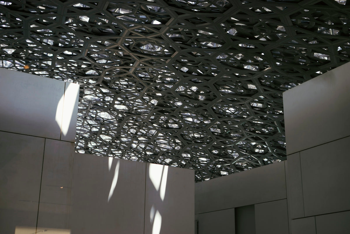Intricate geometric ceiling casting dappled light on modern interior walls.