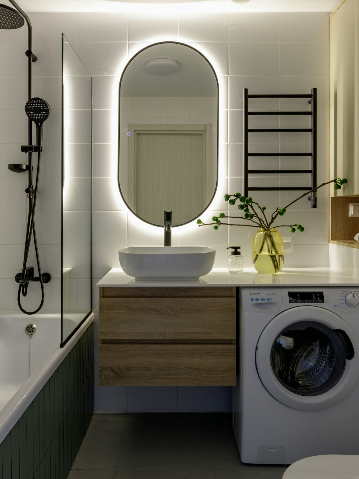 Modern bathroom with backlit mirror, washing machine, and bathtub.