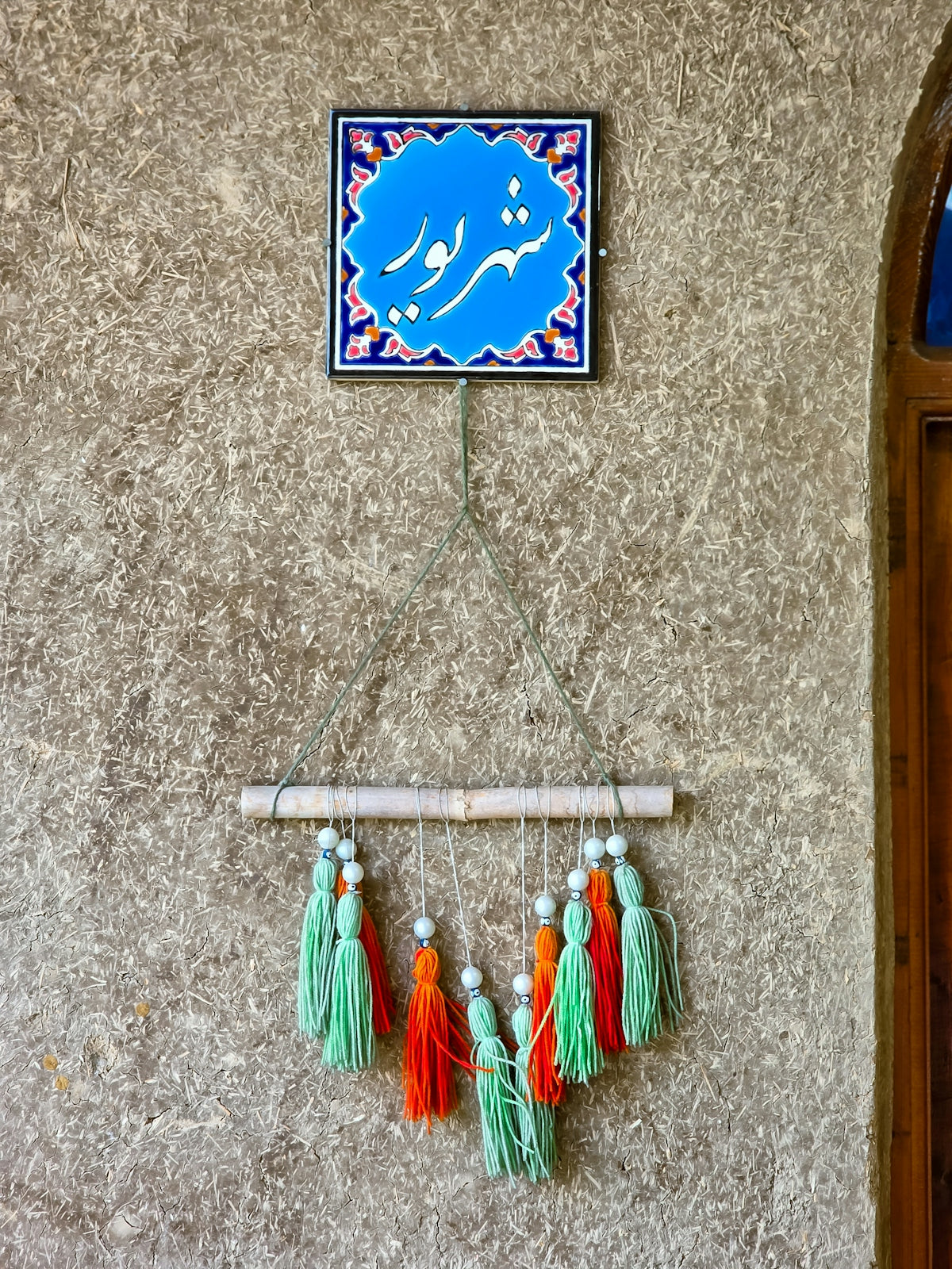 A wall with a blue tiled sign and colorful tassels.