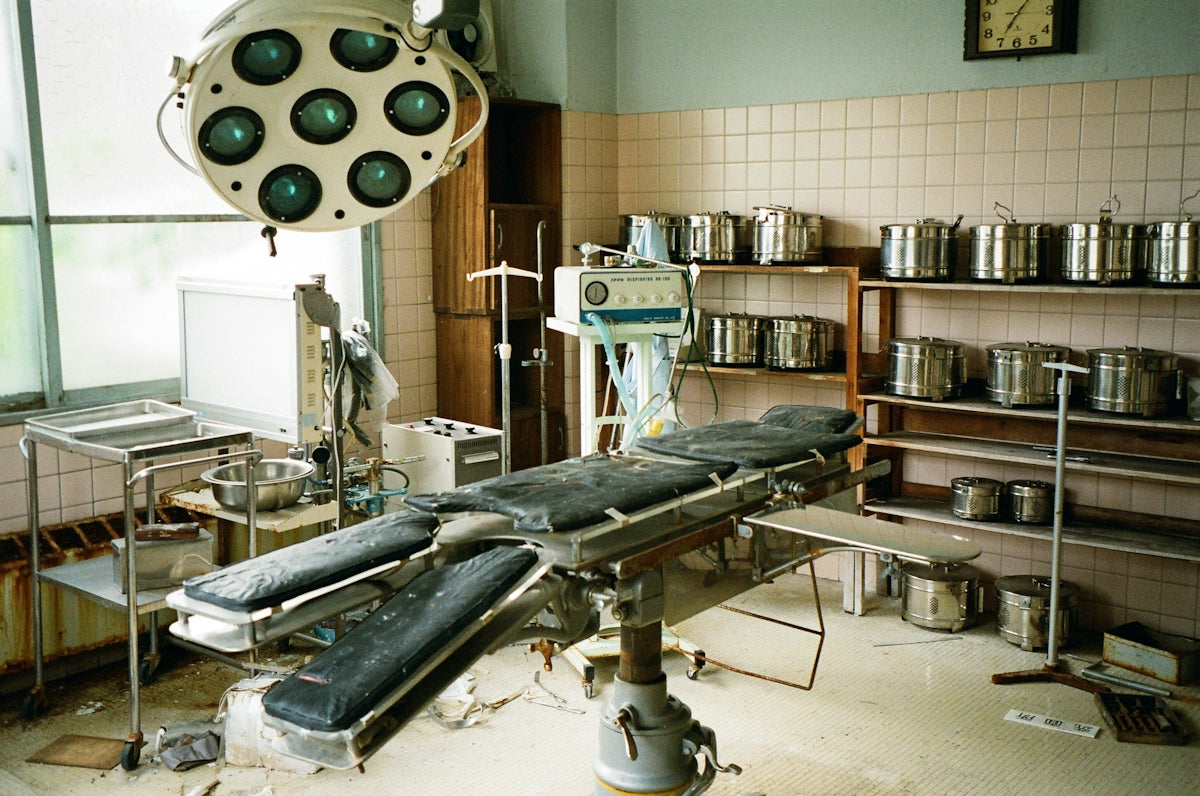 Abandoned operating room with surgical table and medical supplies.